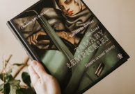 Na zdjęciu książka trzymana w ręce. Na okładce książki ilustracja malarska autorstwa Tamary Łempickiej. Tytuł książki "Śladami Tamary Łempickiej. Tamara oczami Tatiany". Okładka książki w kolorach zielono-granatowych z białymi napisami. Na okładce podpisana również autorka Tatiana de Rosnay, oraz autorka zdjęć Charlotte Jolly de Rosnay.